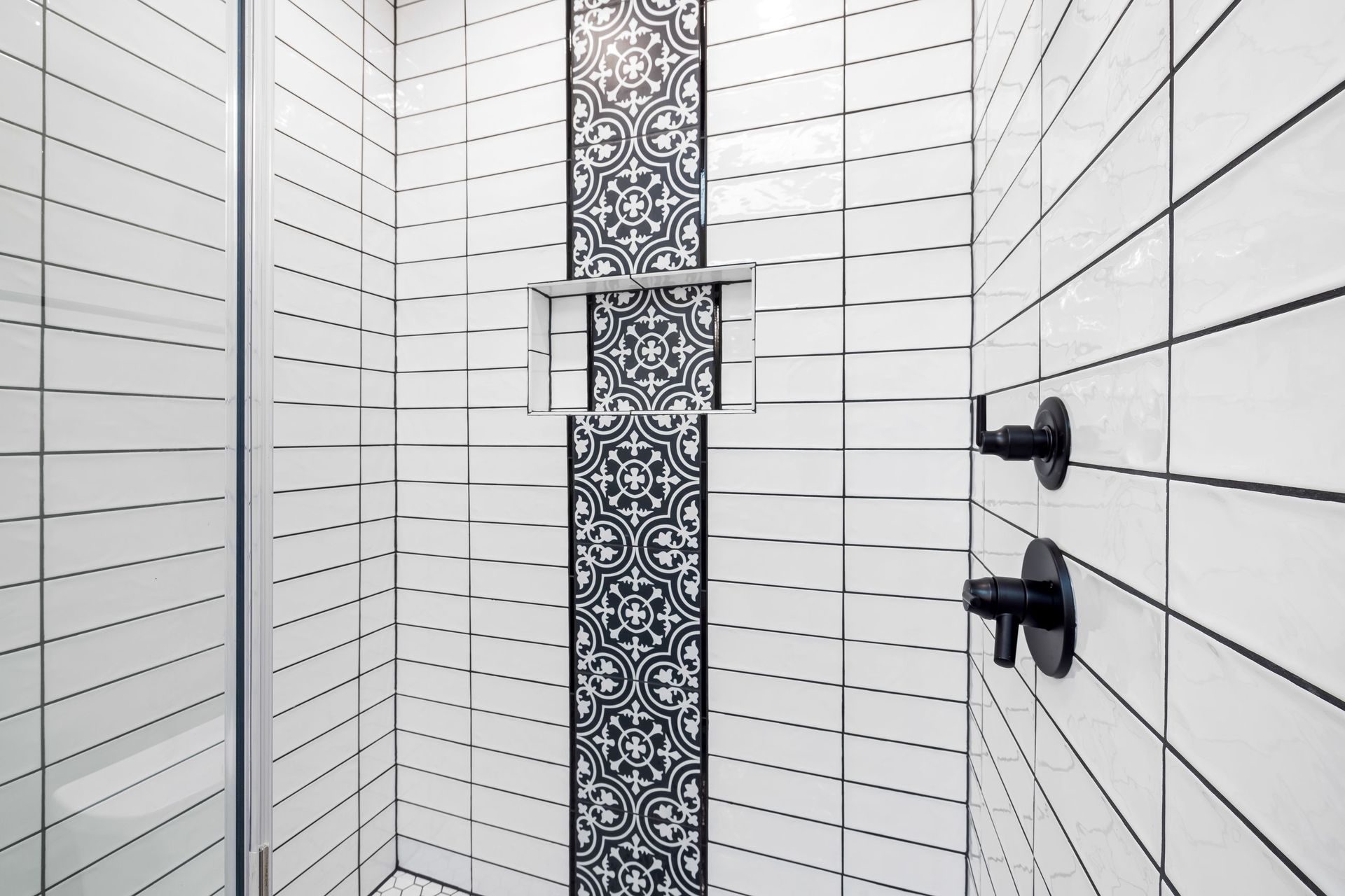 Modern white tile shower with black geometric mosaic accent, niche and matte black fixtures