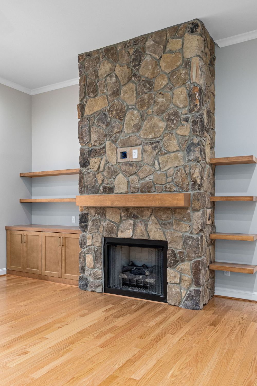 Floor-to-ceiling stacked stone fireplace with wood shelves