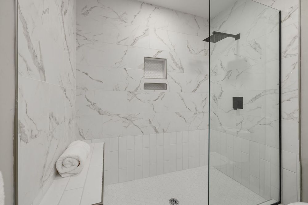 White marble walk-in shower with glass door and bench